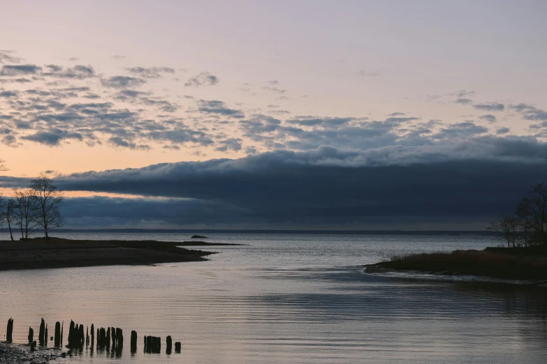 a body of water sitting under clouds near some trees