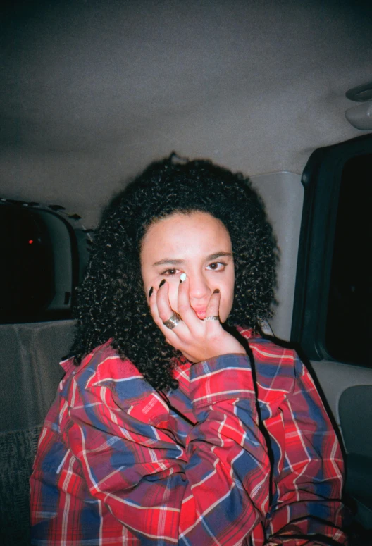 a woman sits in a car, holding her hand up to her face