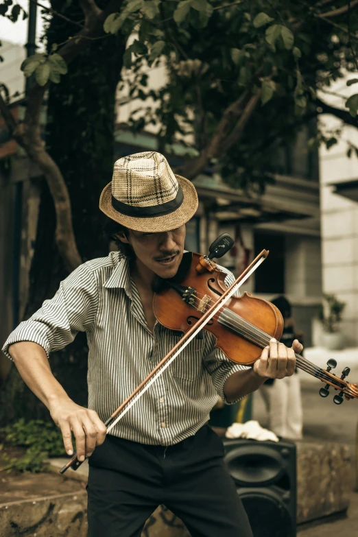 the man is playing his violin outside near the trees