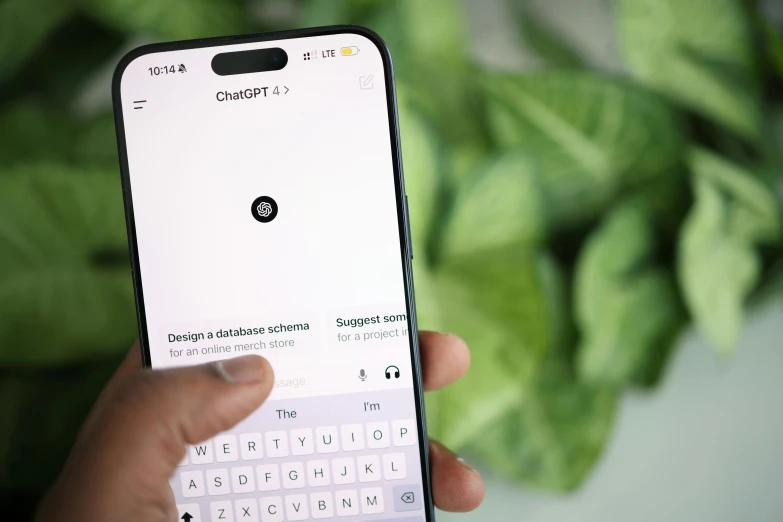 a hand holding up a white cellphone next to plants