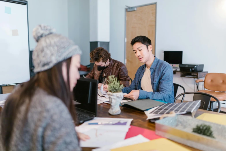 three people are gathered around a table working on laptops