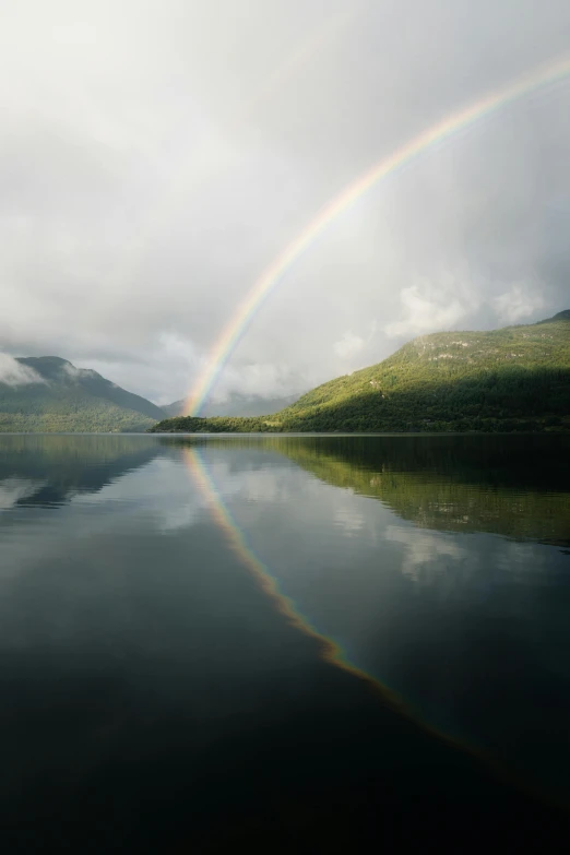 a rainbow is seen over the water with hills in the background