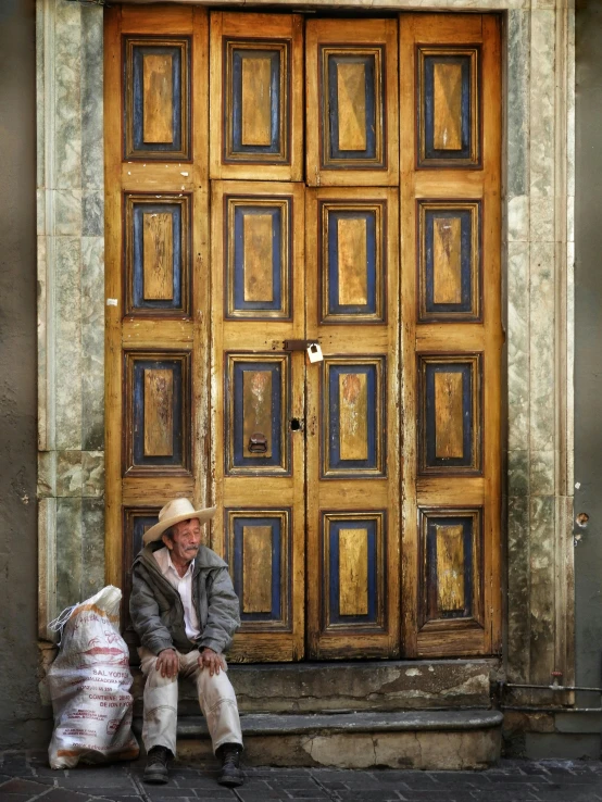 a man sitting on the floor in front of a building with doors painted gold