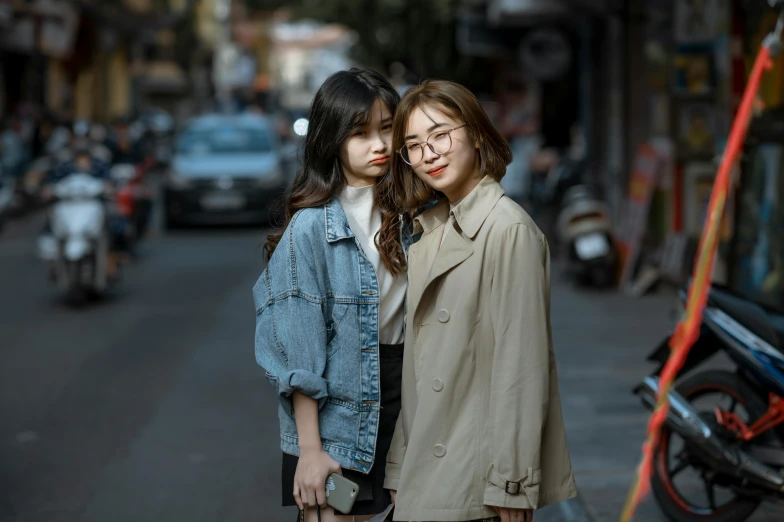 two asian girls standing on a street by motorcycles