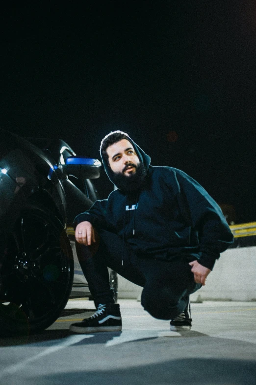 man squatting down to pose next to a motorcycle