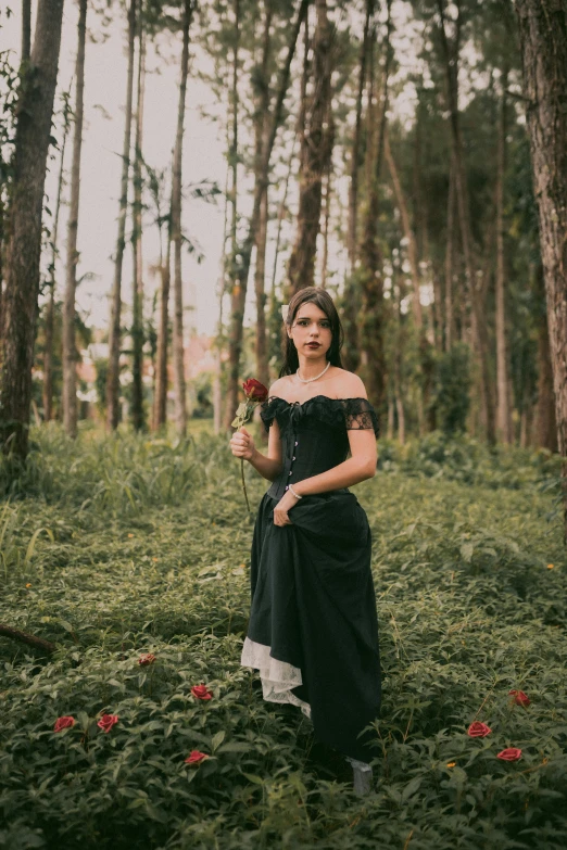 a woman holding a rose and standing in a forest