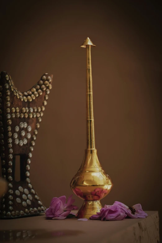 a golden vase with pink flowers on a shelf