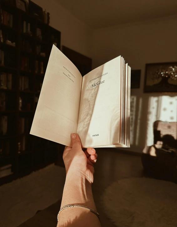 someone holding a book in their hands near a book case