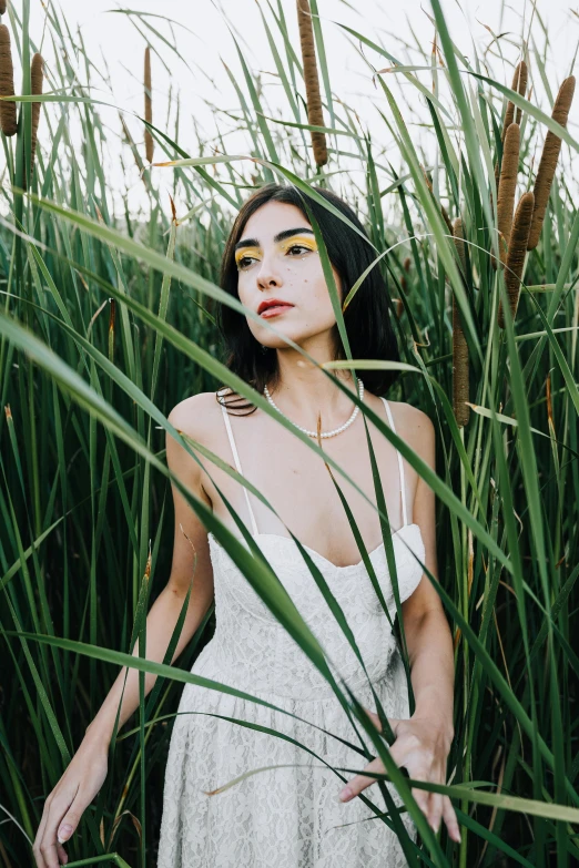 a woman standing in tall grass with yellow eyeshadow