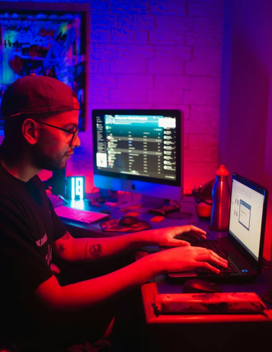 a man in glasses at a desk with a laptop and computer