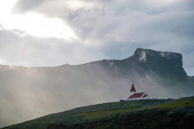 a red house is on top of the hill with a mountain in the background