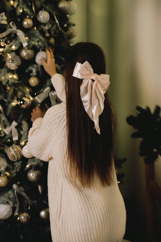 a young woman with a bow is standing near a christmas tree