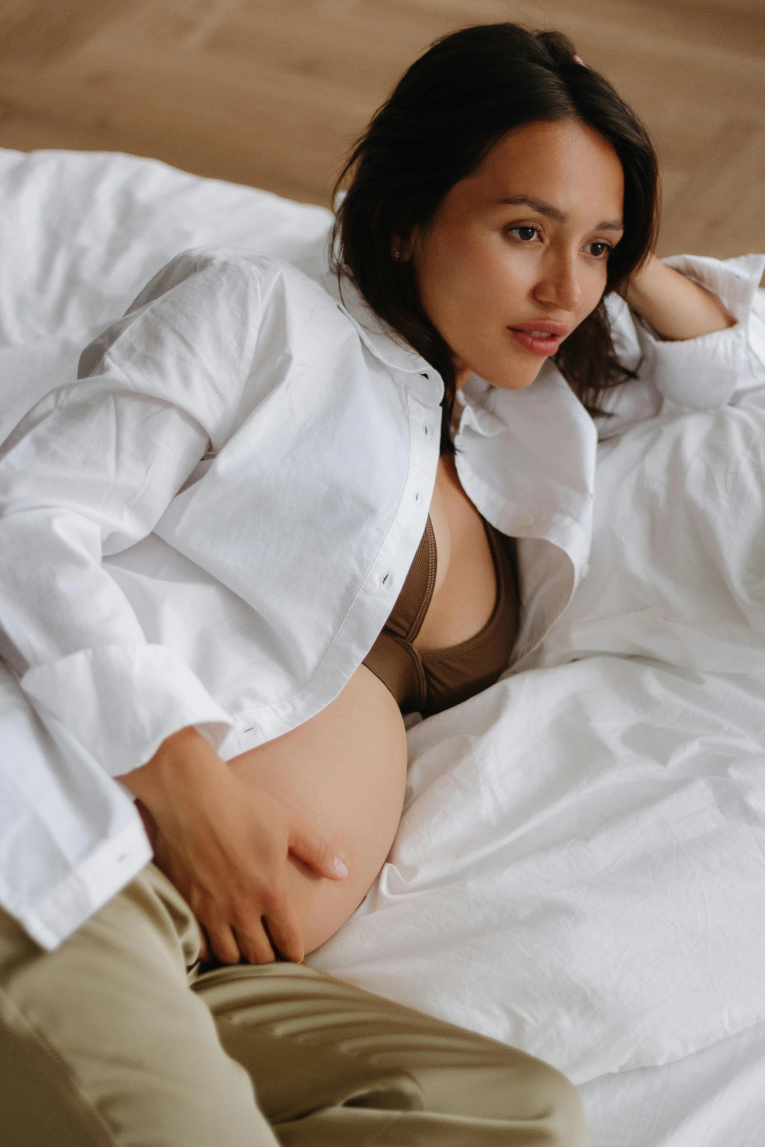 a woman laying in bed wearing an oversize white shirt