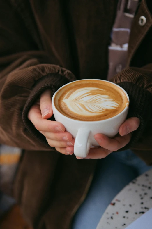 person holding a cup of art coffee in their hands