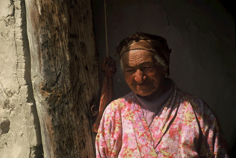 an old woman is standing by a tree with a rope