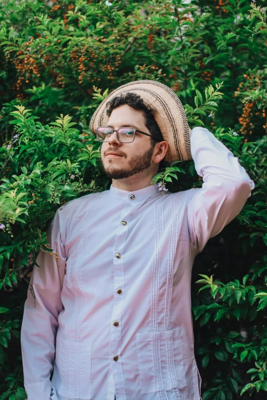 a man wearing a straw hat poses by some trees