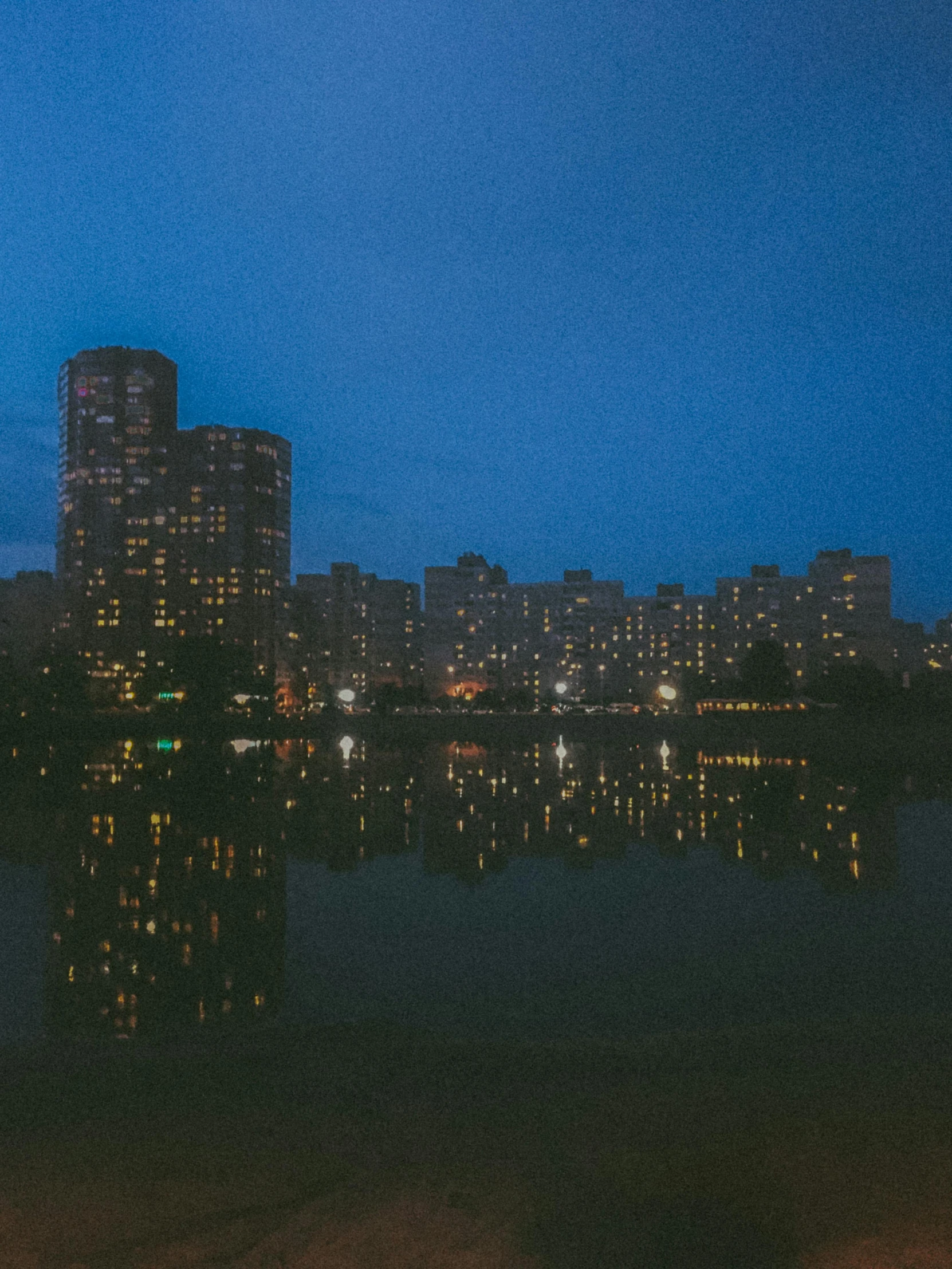 the night city lights reflect in the calm water