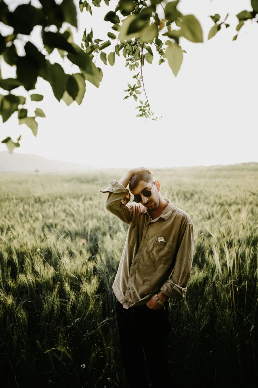 a man in sunglasses and a brown shirt standing in a field