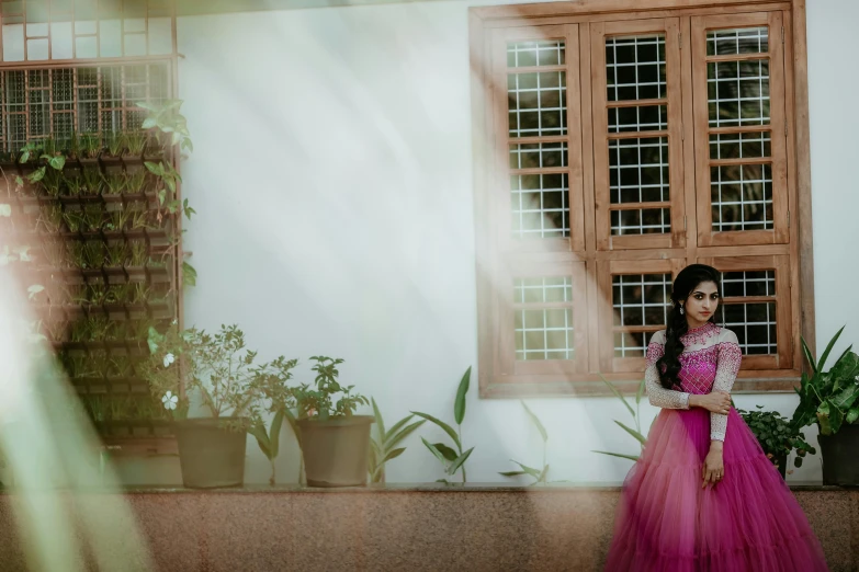 young woman dressed in long pink skirt standing near window