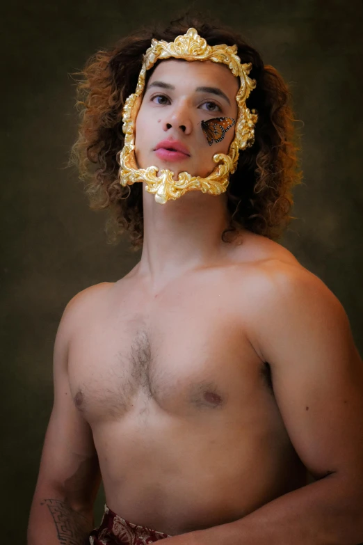 a shirtless man with a gold mask covering his face