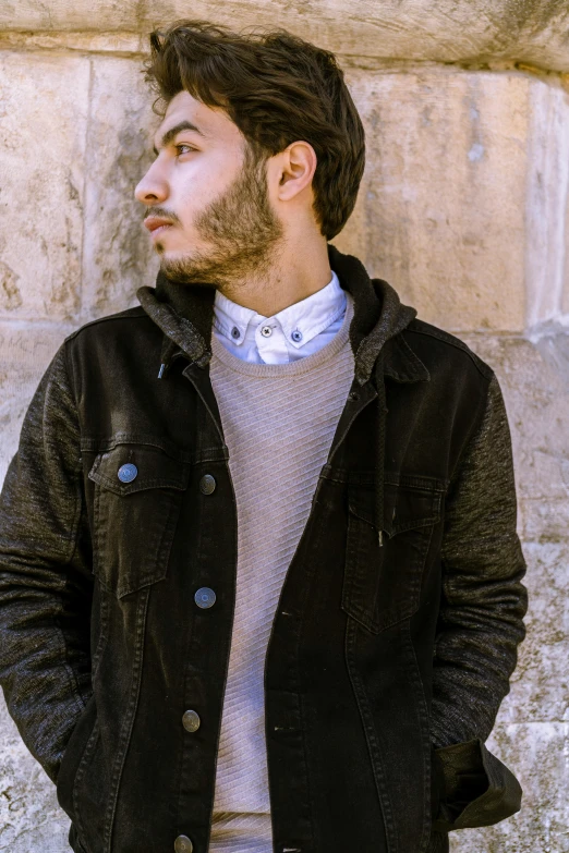 a young man standing by a wall wearing a coat