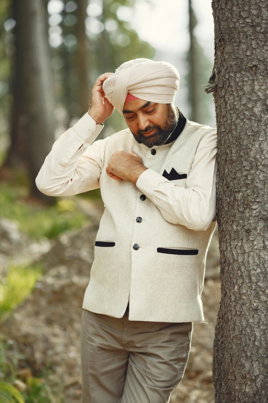 a man wearing a turban leaning against a tree
