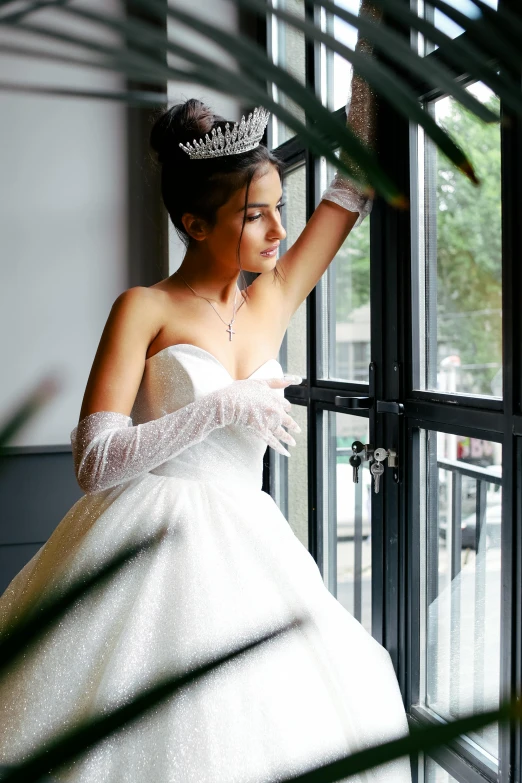 a bride in white wedding dress looking out a window