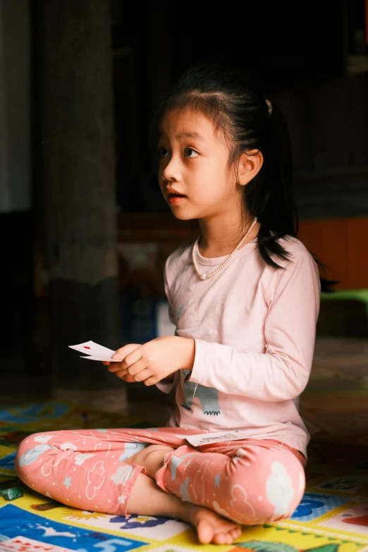 the little girl sitting on the floor holds a remote