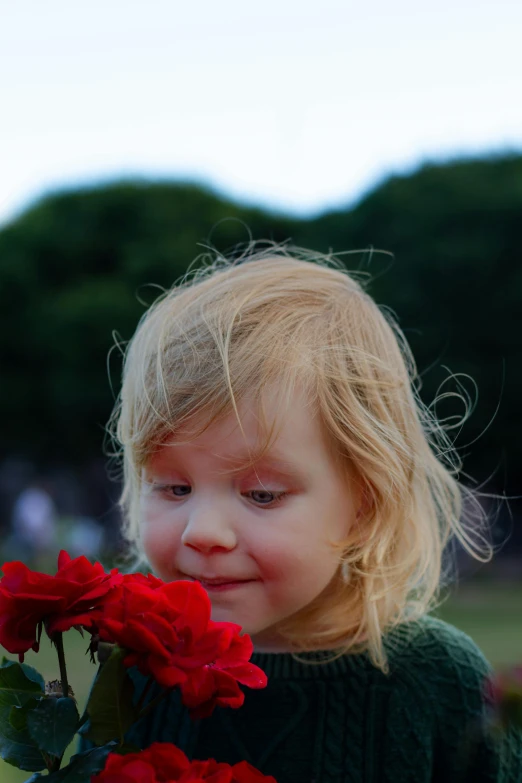 a girl holding flowers in her hands with trees and bushes behind her