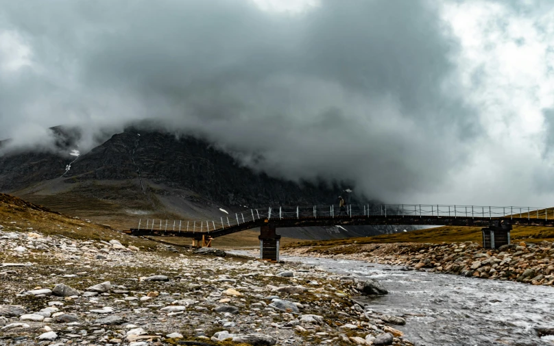 a bridge crosses a rocky river surrounded by a mountain