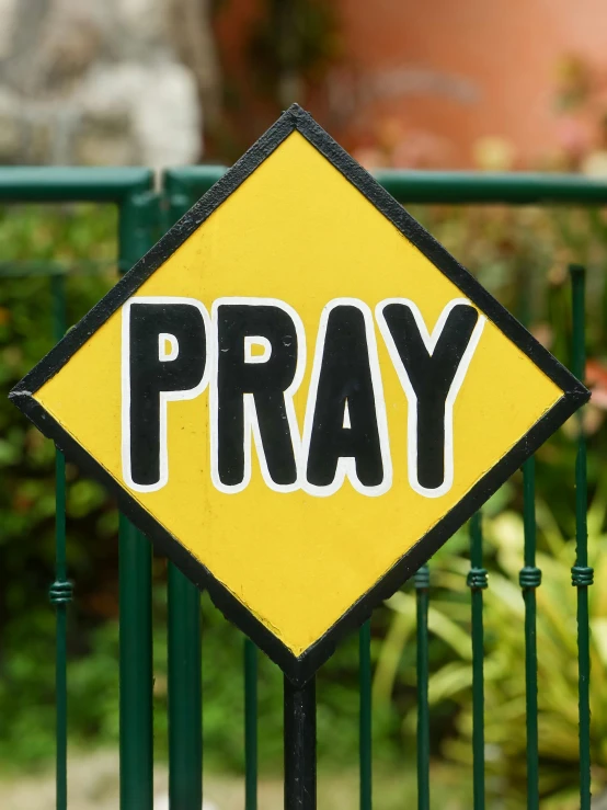 a yellow sign reading pray on it sitting on top of green poles