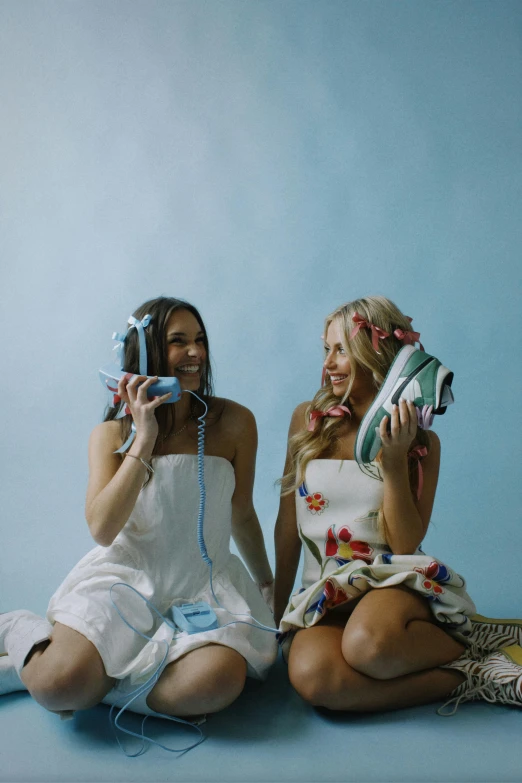 two women sitting on the ground while talking on telephones