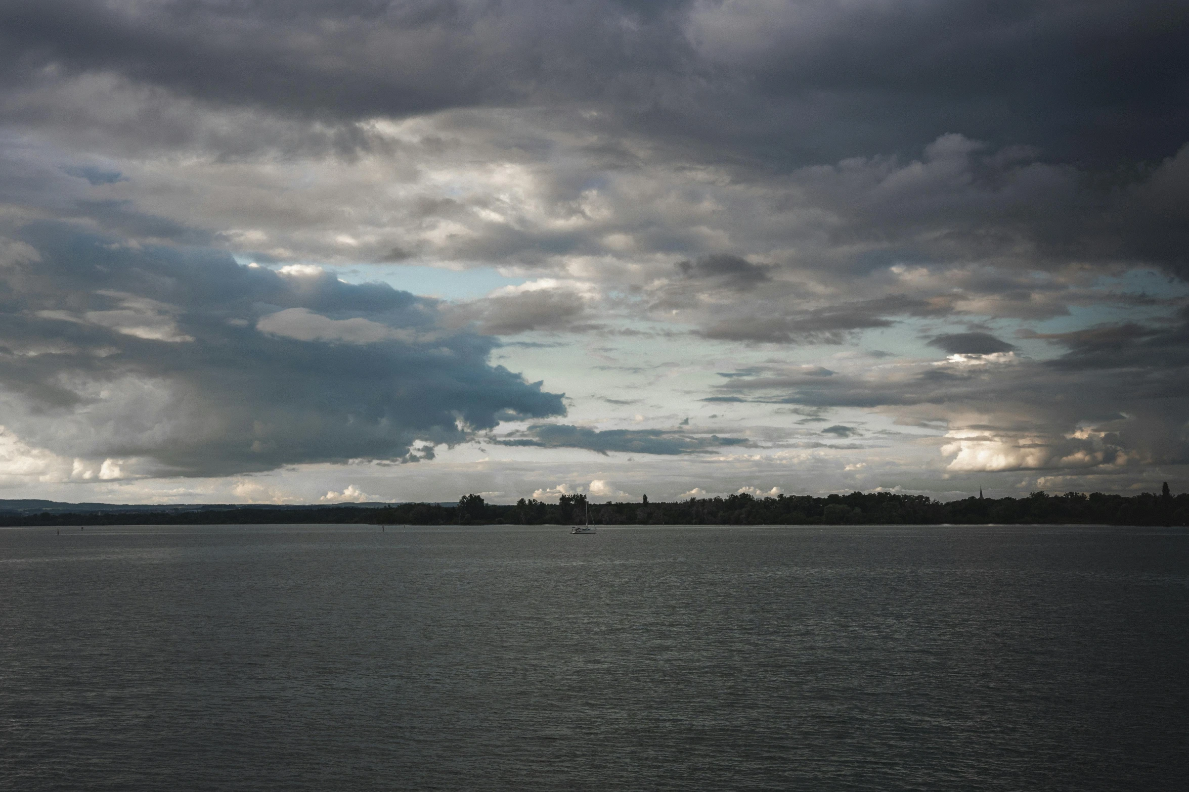 a sail boat floating on a large lake under dark clouds