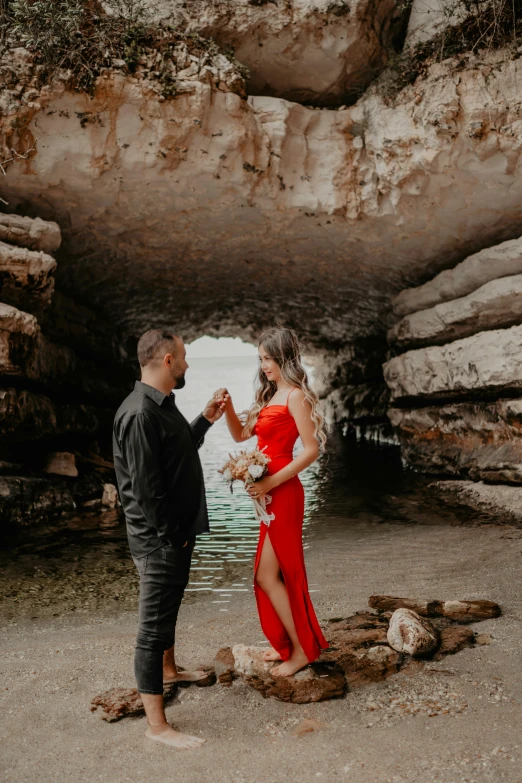 the man and woman are standing in front of a cave