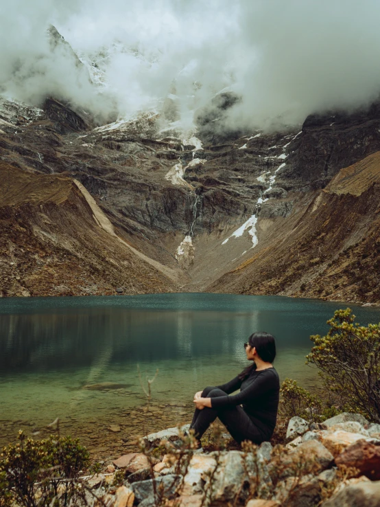 a man sitting on rocks looking out at mountains