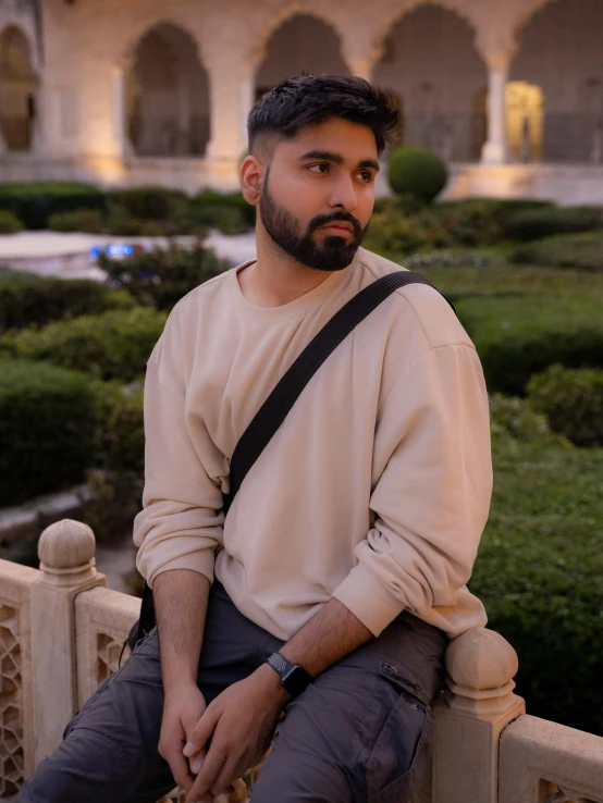 a bearded man sitting on a gate holding a camera