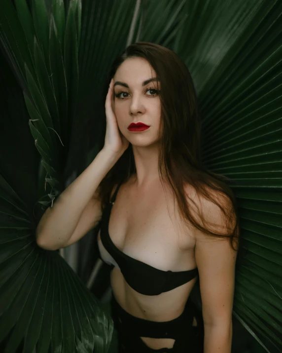 a woman with her hands on the face and her arms behind her head, posing for a po with large palm leaves