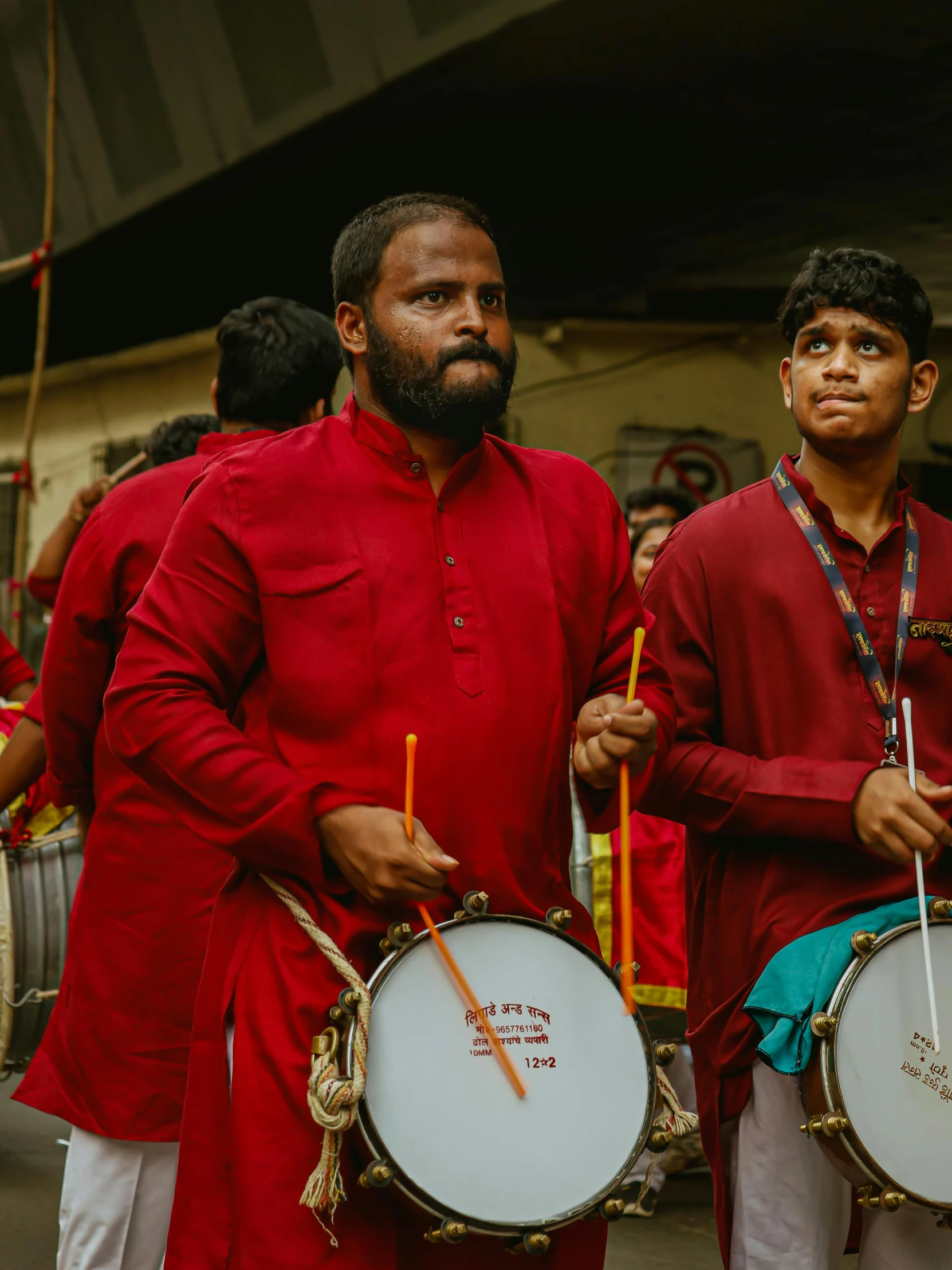 two men wearing red are holding drum strings