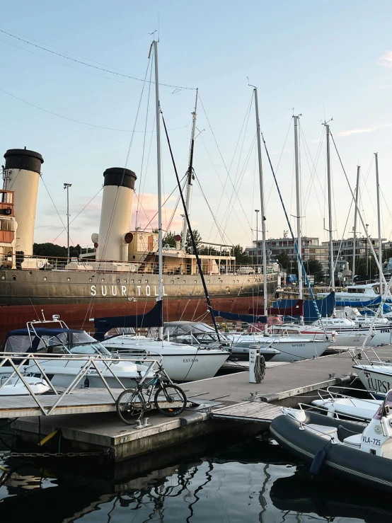 many sailboats are parked at the docks near a large ship