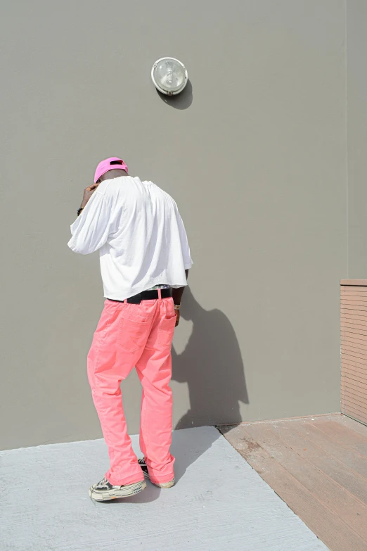 a man wearing a white t - shirt and pink sweatpants standing next to a wall with a disk on it