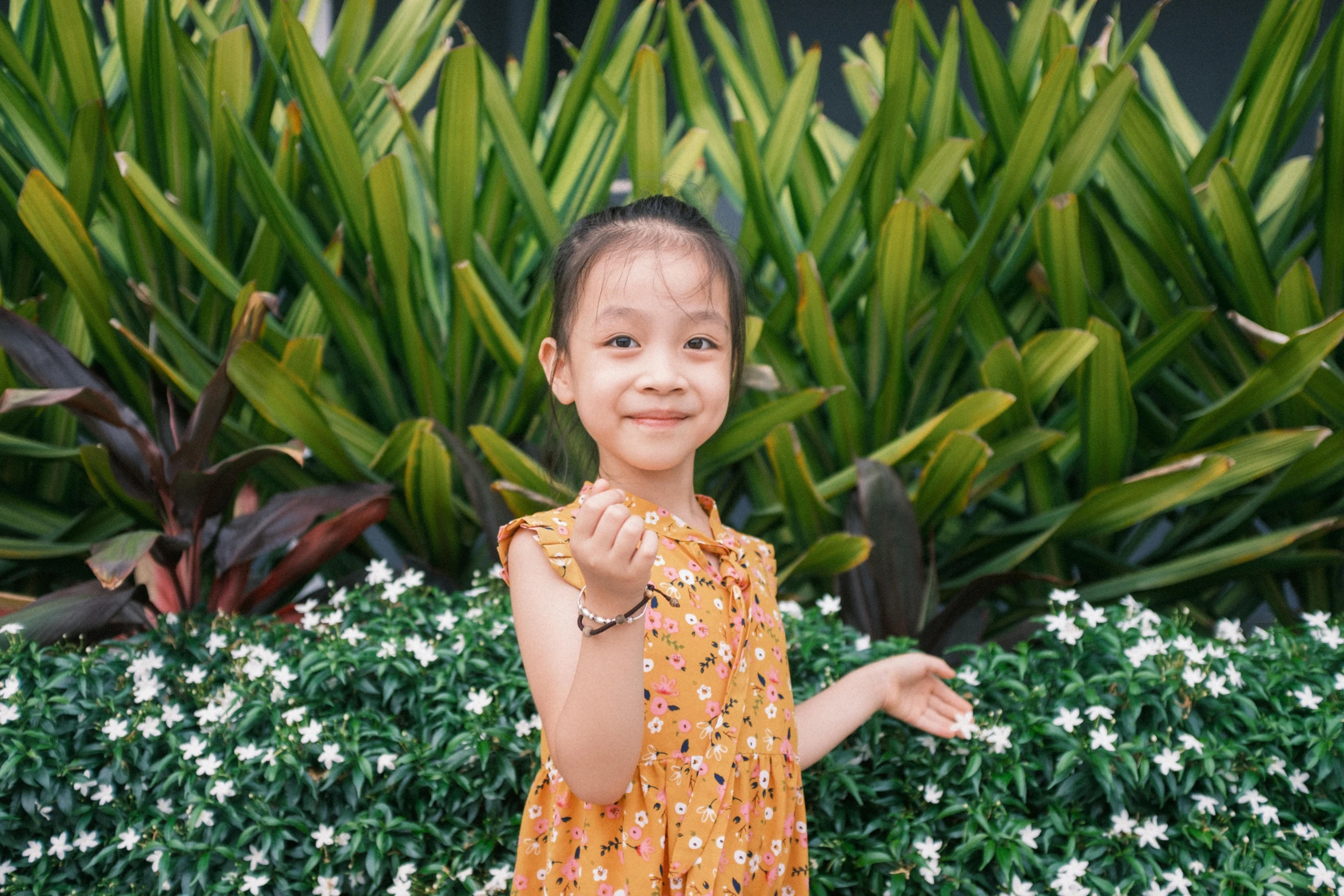 little girl in yellow dress standing next to plants