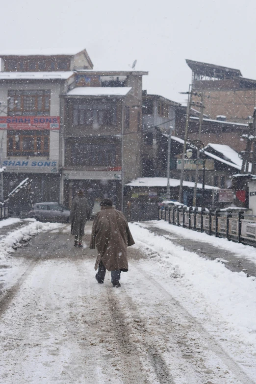 people are walking down a snowy street by a large building