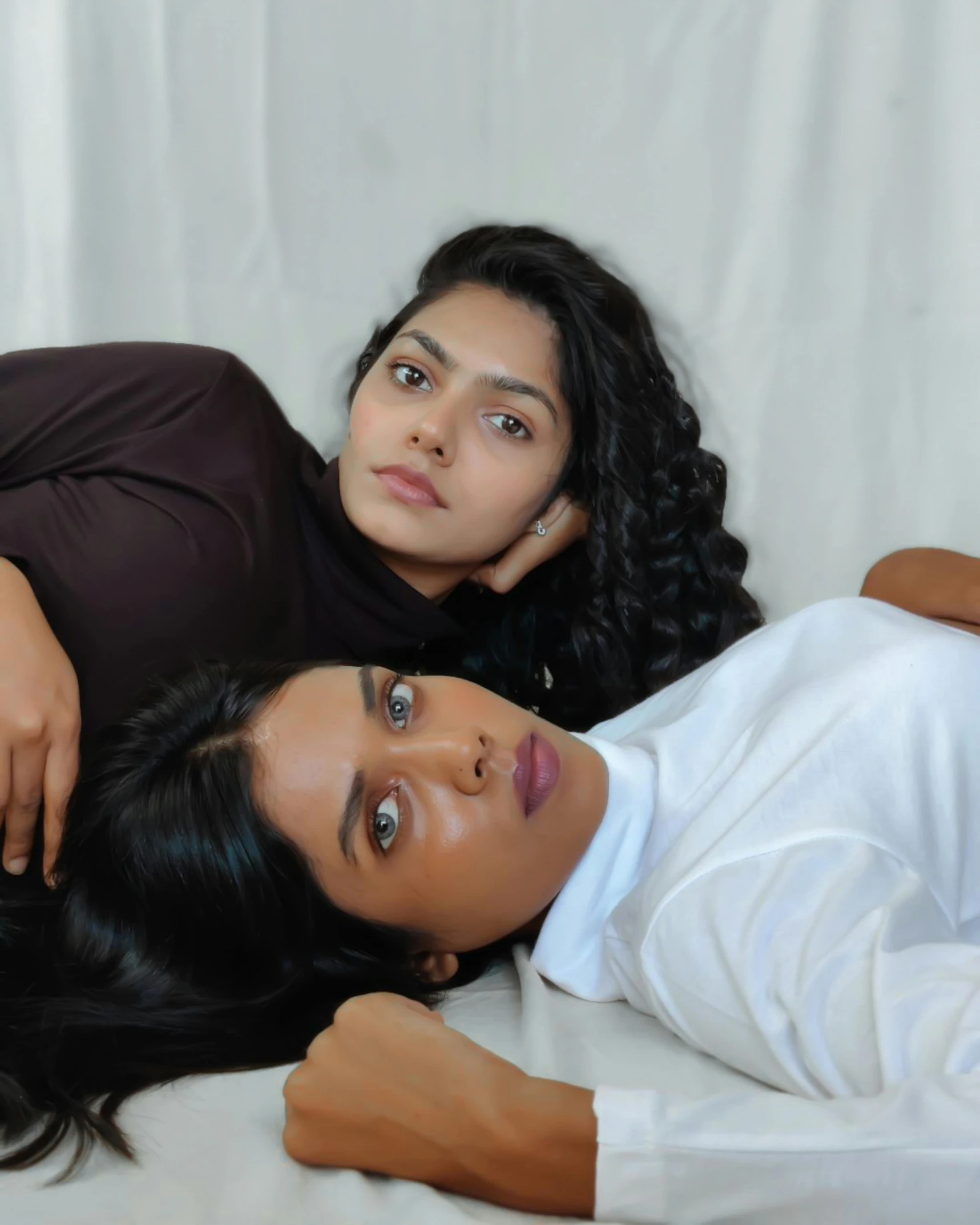 two women laying on a bed one has an earring