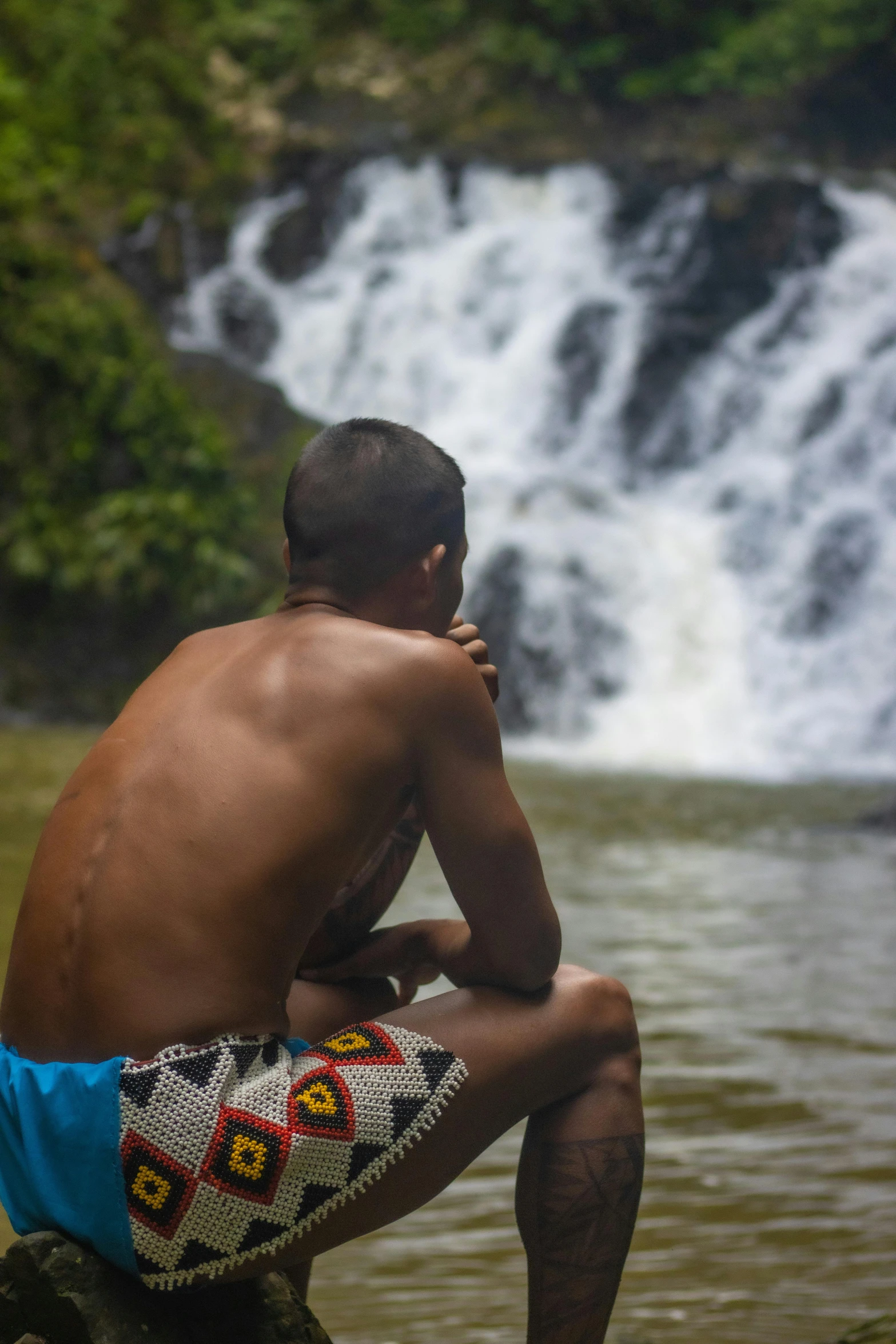 the man is sitting on a rock in front of the waterfall