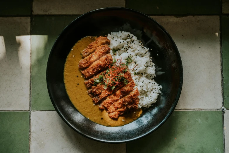 a black bowl filled with rice, meat and curry