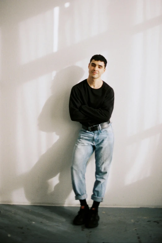 a young man in black shirt standing against a white wall