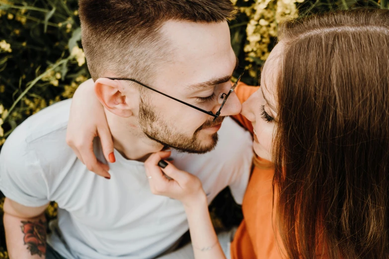 a man in glasses and woman in orange are holding their foreheads together