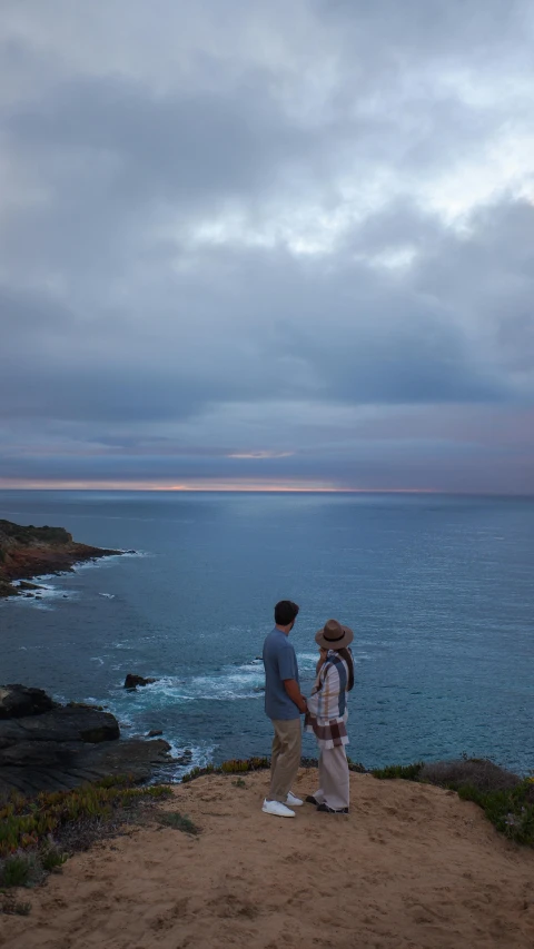 there is a couple of people standing near the ocean