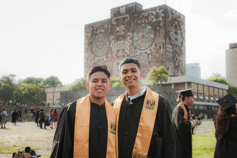 two men in graduation caps and gowns stand on the grass