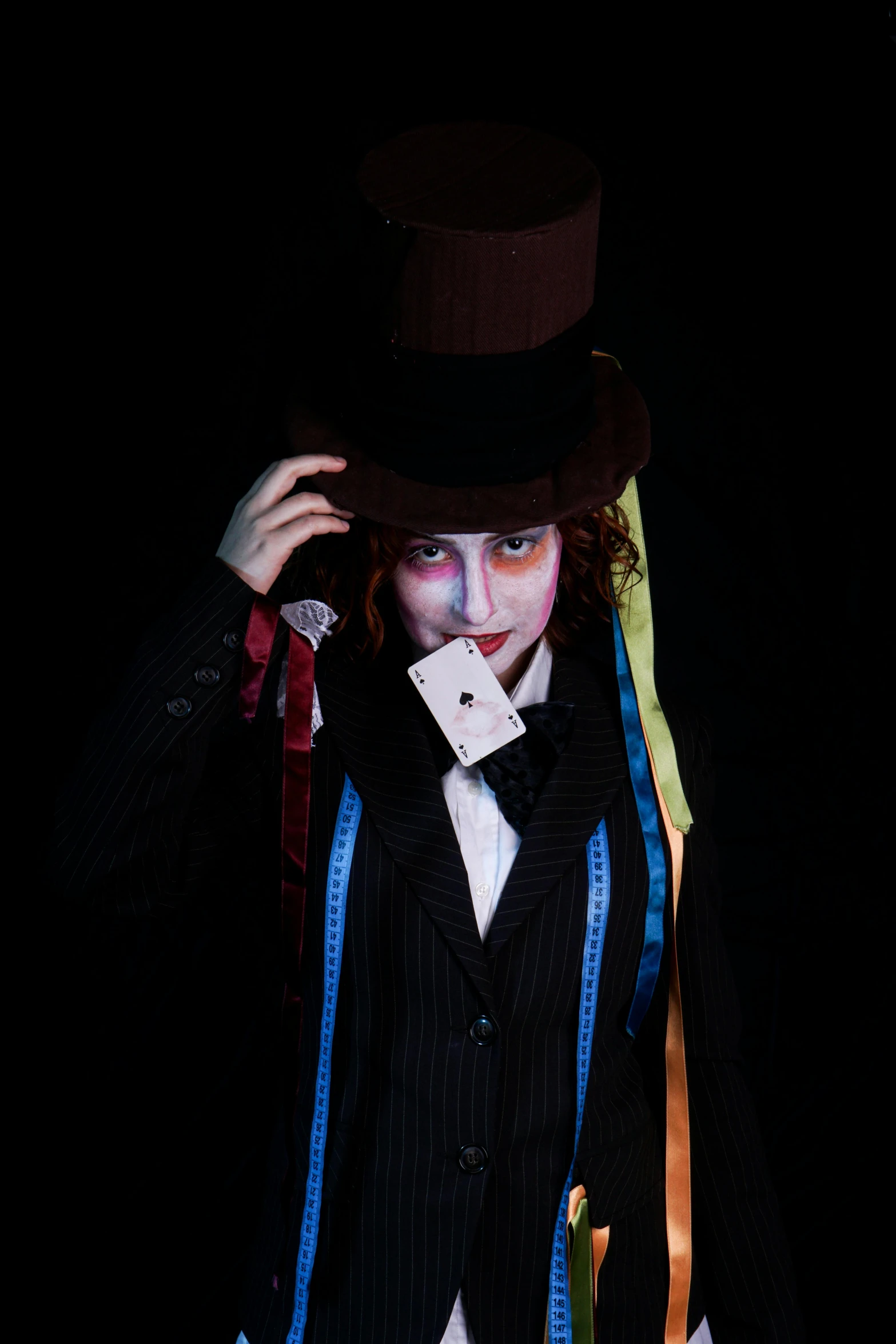 a clown in top hat and tie holding his face covered